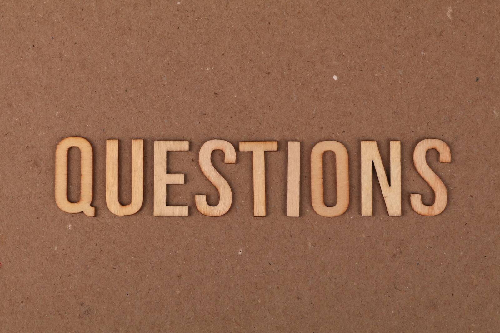 Wooden letters spelling the word "QUESTIONS" on a cardboard background, providing a neutral copyspace.
