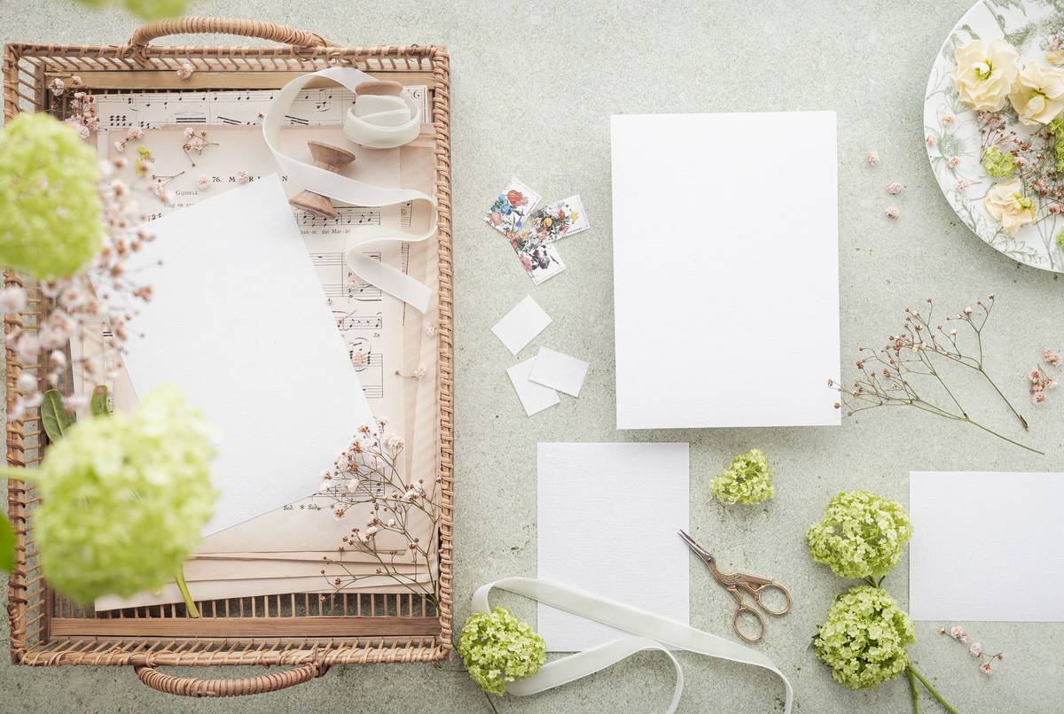A styled flat lay featuring wedding invitations with green floral accents and stationery items.