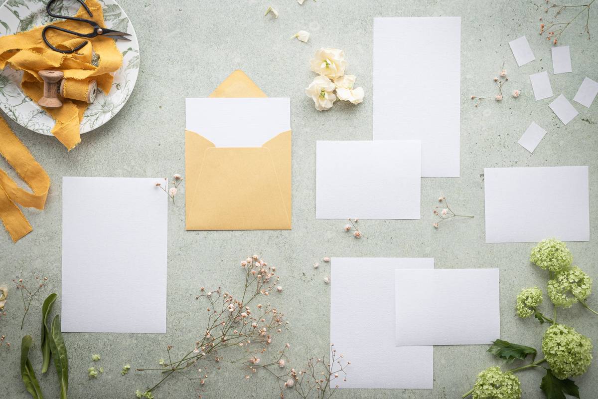 A flat lay of blank stationery and envelope amidst delicate flowers and ribbon, perfect for wedding or event planning.