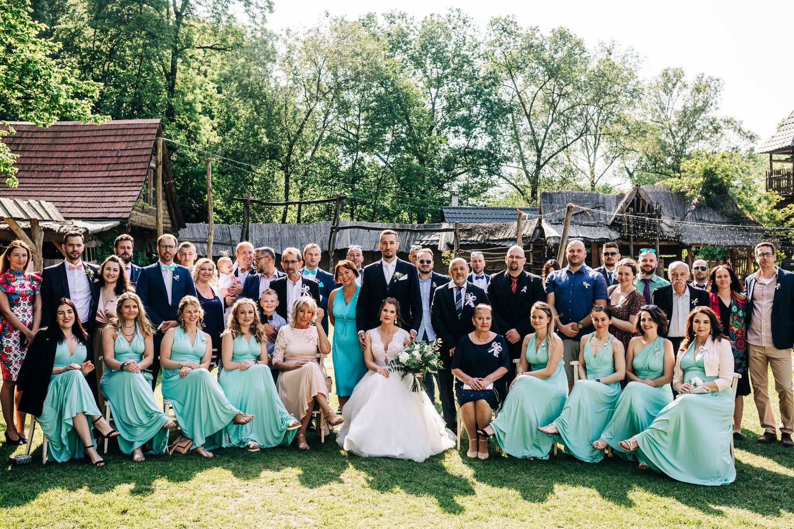 Large group photo of wedding guests outdoors on a sunny day.