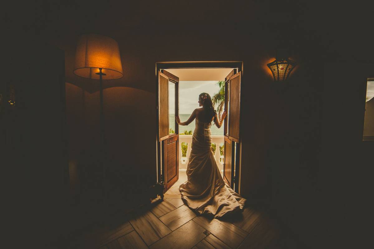 A bride stands silhouetted in a doorway, gazing towards the sunset outside.
