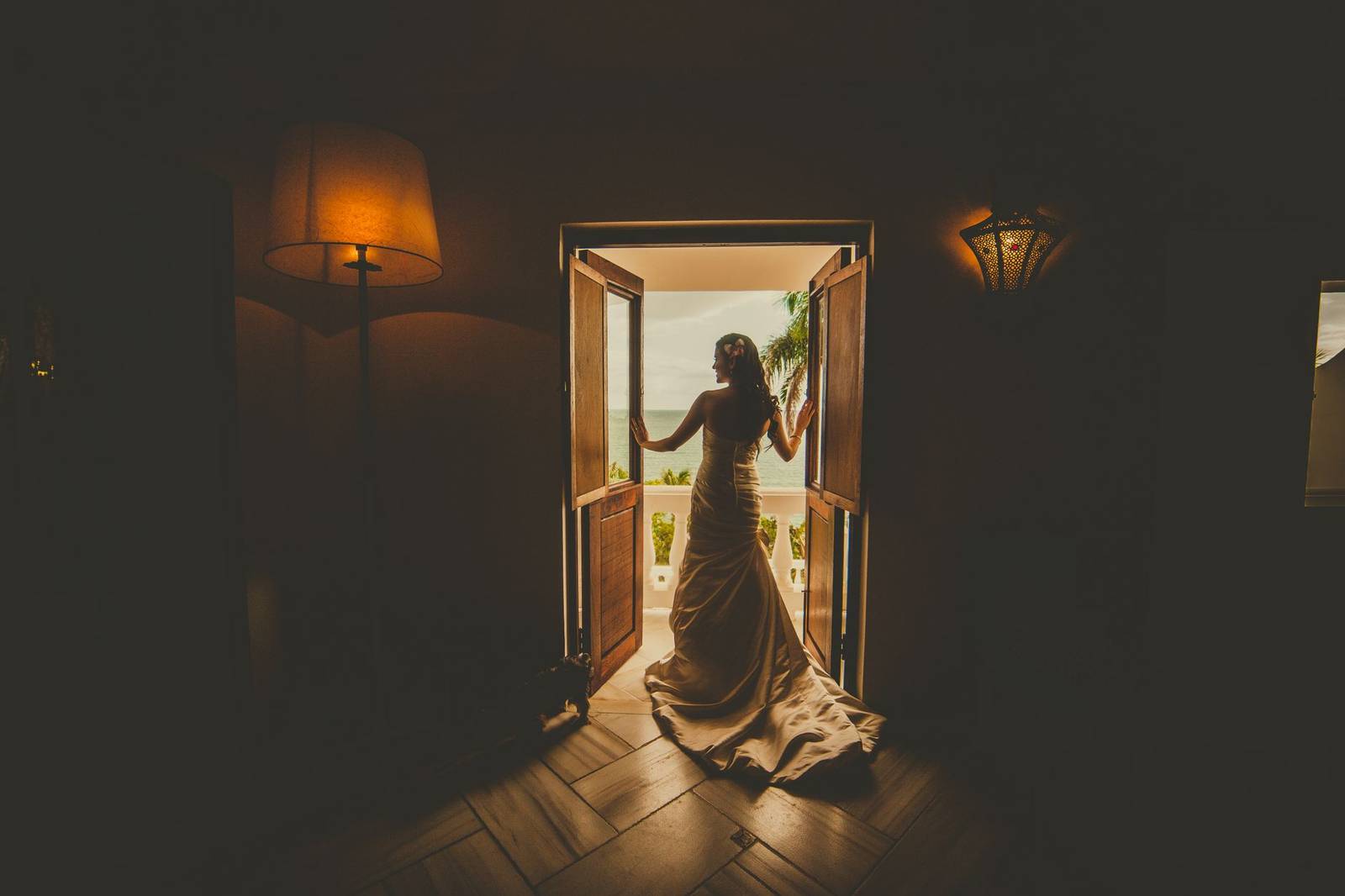 A bride stands silhouetted in a doorway, gazing towards the sunset outside.