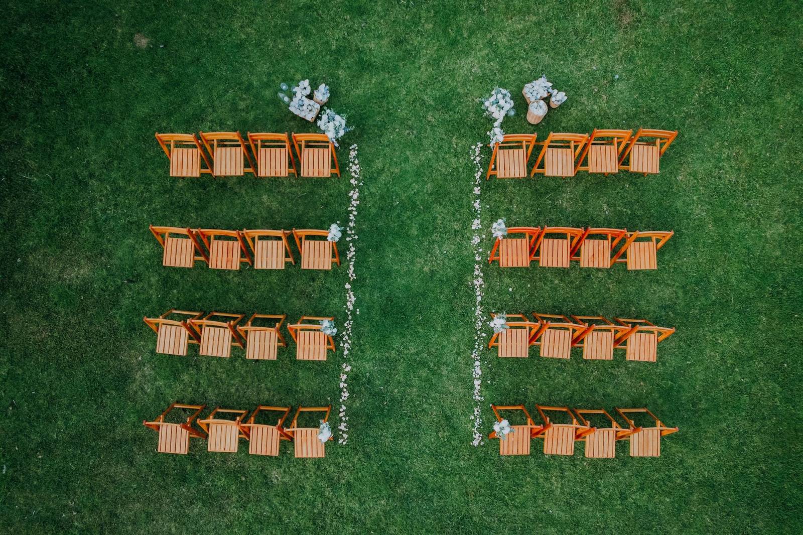 Drone shot of a wedding seating arrangement with orange chairs on green grass.