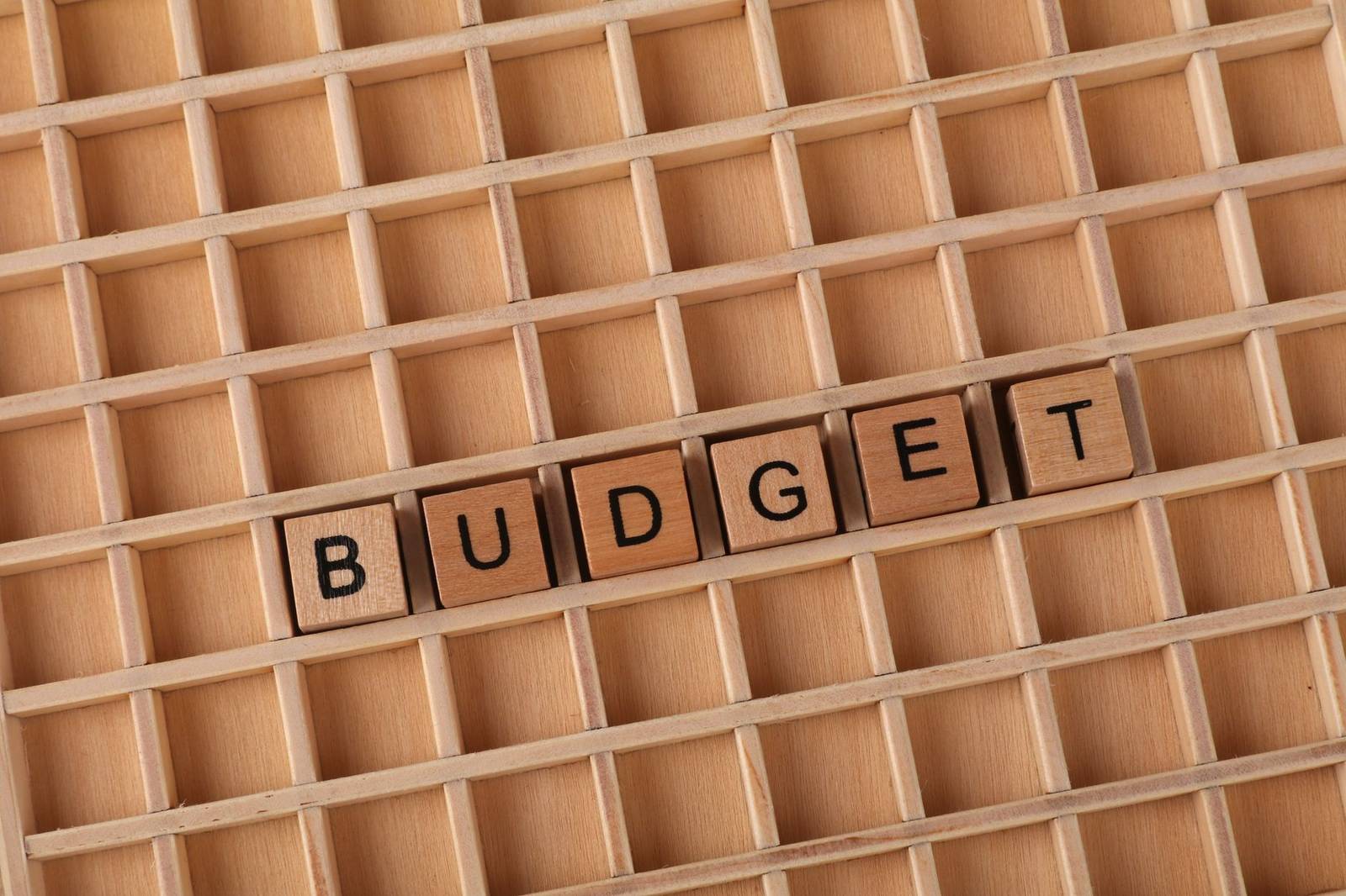 Wooden letter tiles spelling 'budget' on a wooden grid background, symbolizing finance and planning.