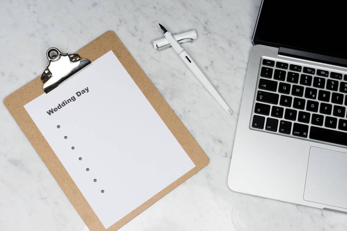 Flat lay of a wedding planning setting with clipboard, laptop, and pen.