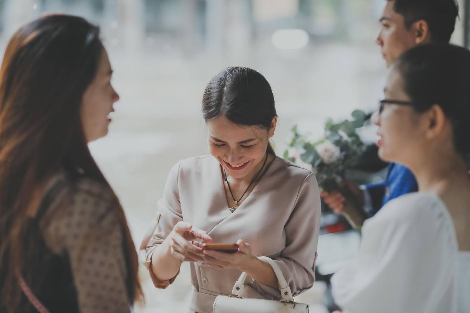 Women socializing and using a phone at a wedding event, creating connections with a joyful atmosphere.